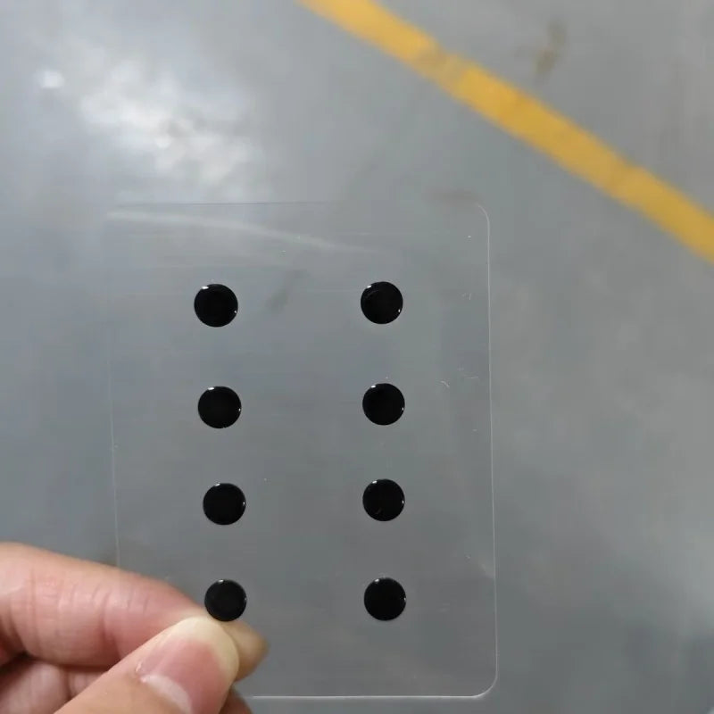 A hand is placing small black circular items onto a clear plastic sheet for DIY mouse skates.