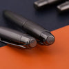 Two black metal ballpoint pens resting on an orange surface.