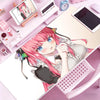 A close-up of a pink-haired anime girl relaxing on a desk with various stationery and a tablet nearby.