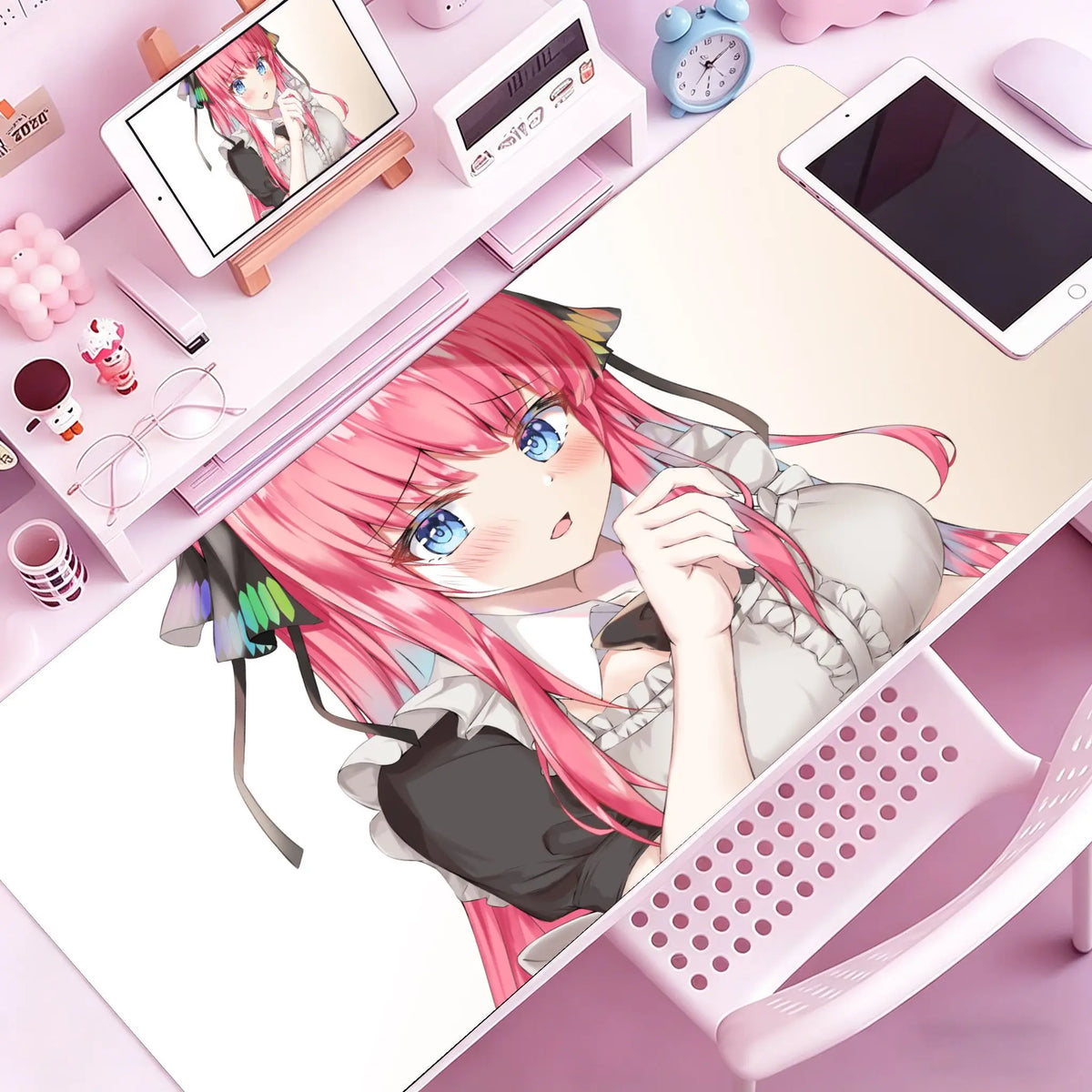 A close-up of a pink-haired anime girl relaxing on a desk with various stationery and a tablet nearby.