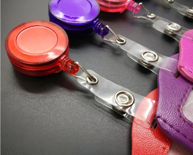 A close-up of a retractable ID card holder with various colored badge cases attached to clear plastic reels.