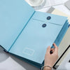 A hand is opening a light blue expanding accordion document organizer file folder on a white surface.
