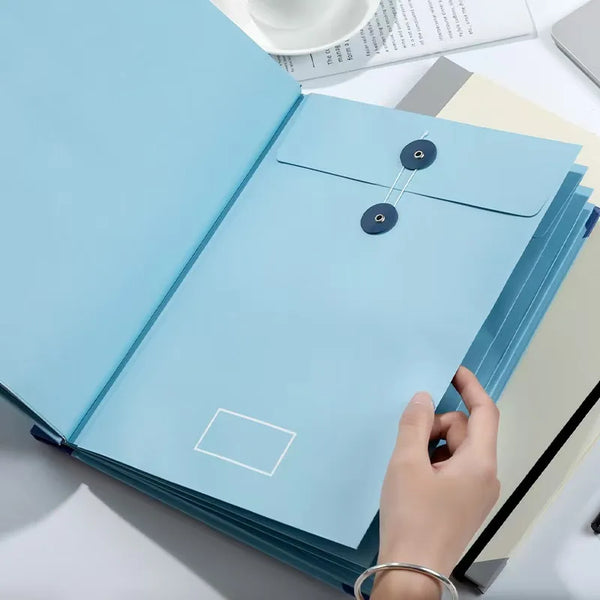 Eine Hand öffnet eine hellblaue, ausklappbare Akkordeon-Dokumentenmappe auf einer weißen Oberfläche.