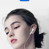 A close-up of a woman wearing white wired in-ear earphones with a white cord against a light background.