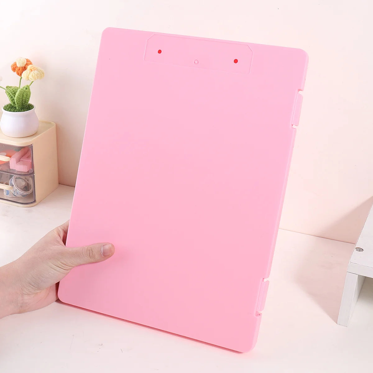 A pink A4 document and photo storage file box being held by a hand on a white surface.