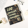 A black marble budget binder titled 100 Envelope Savings Challenge resting on a white surface.