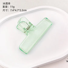 A clear acrylic file clip used for desk organization, shown on a white surface.