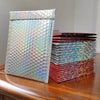 A stack of rainbow foil bubble mailers in various colors, including iridescent and metallic shades.