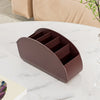 A dark brown remote control holder and desk organizer tray with multiple slots resting on a white marble surface.