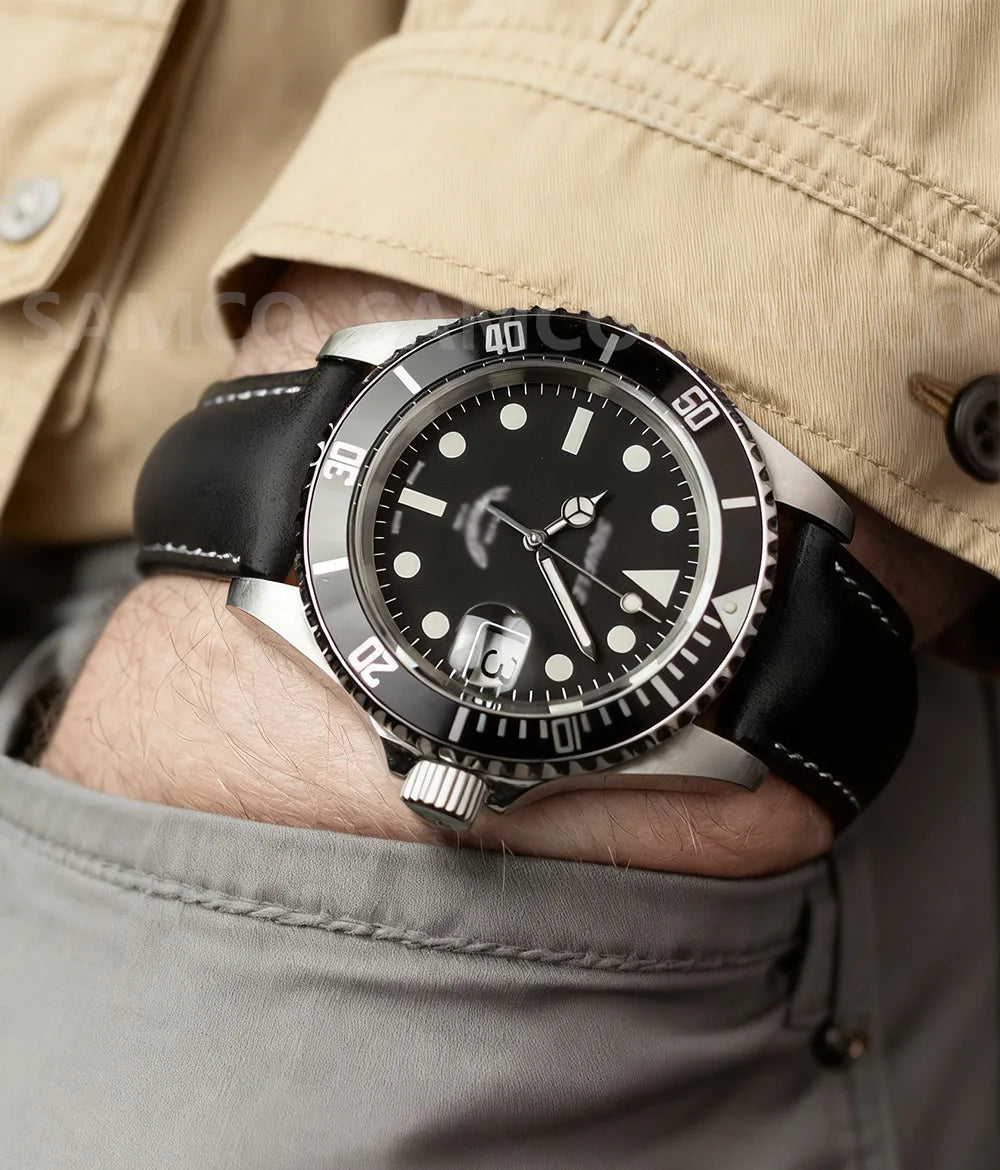 A close-up of a black watch with a silver bezel and leather band worn on a wrist, visible under a beige jacket sleeve.