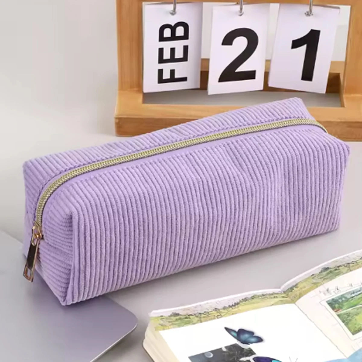 A lavender pencil case with a gold zipper is shown next to a wooden frame displaying the date February 21.