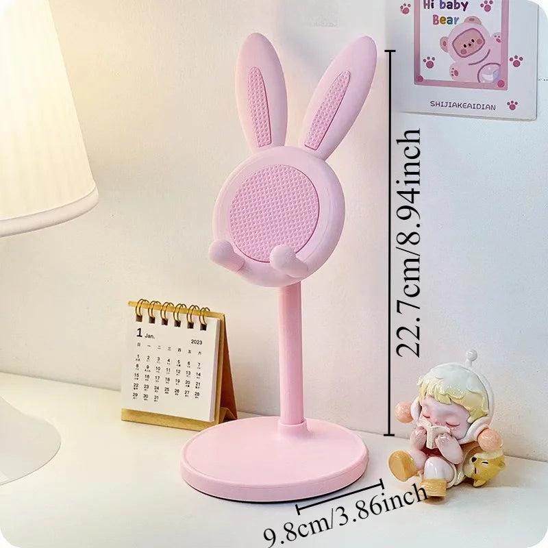 A pink rabbit mobile phone stand with a flat base and upright ears is shown on a white surface.