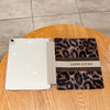 A white tablet is shown with a leopard print protective case featuring the text GOOD LUCKY on the cover, resting on a wooden 