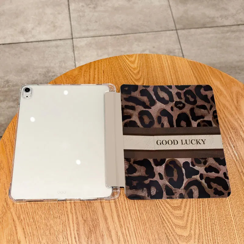 A white tablet is shown with a leopard print protective case featuring the text GOOD LUCKY on the cover, resting on a wooden 