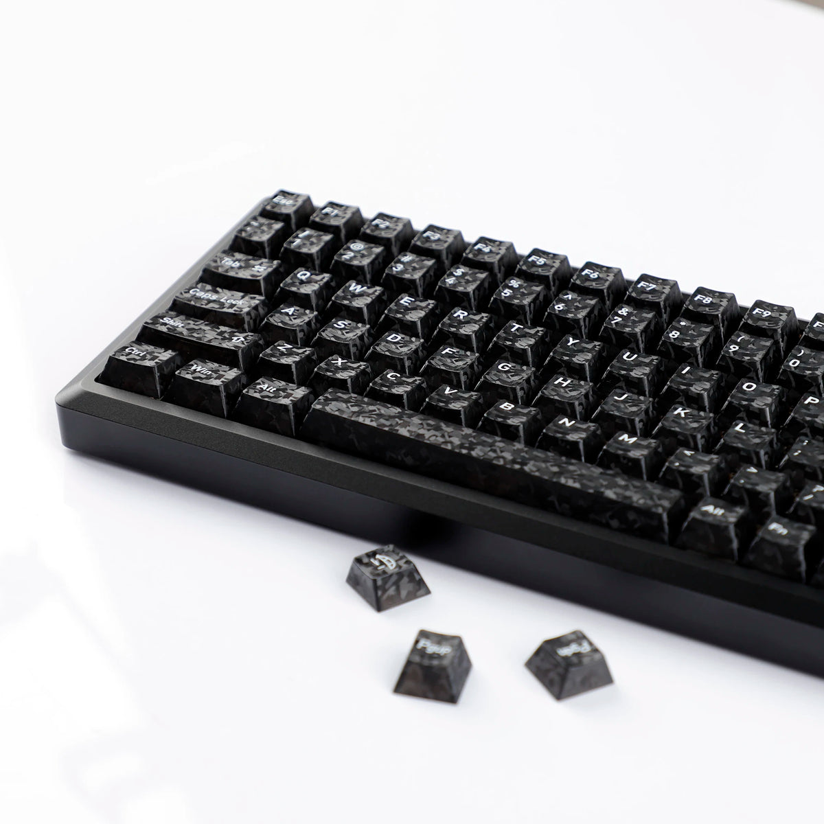 A close-up view of black carbon fiber texture keycaps for MX Mechanical keyboards lying on a white surface.