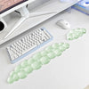A light green ergonomic cloud wrist rest for keyboard and mouse placed on a white desk next to a computer setup.