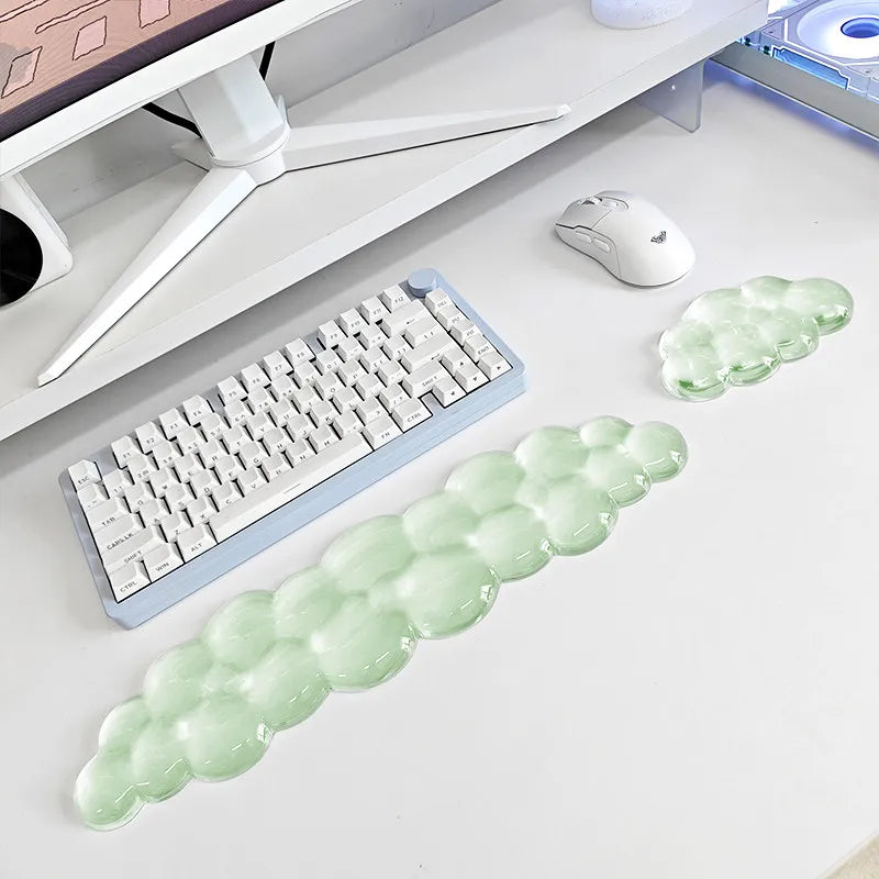 A light green ergonomic cloud wrist rest for keyboard and mouse placed on a white desk next to a computer setup.