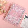 A clear plastic envelope containing a pink patterned savings challenge journal and a white calculator on a pink background.