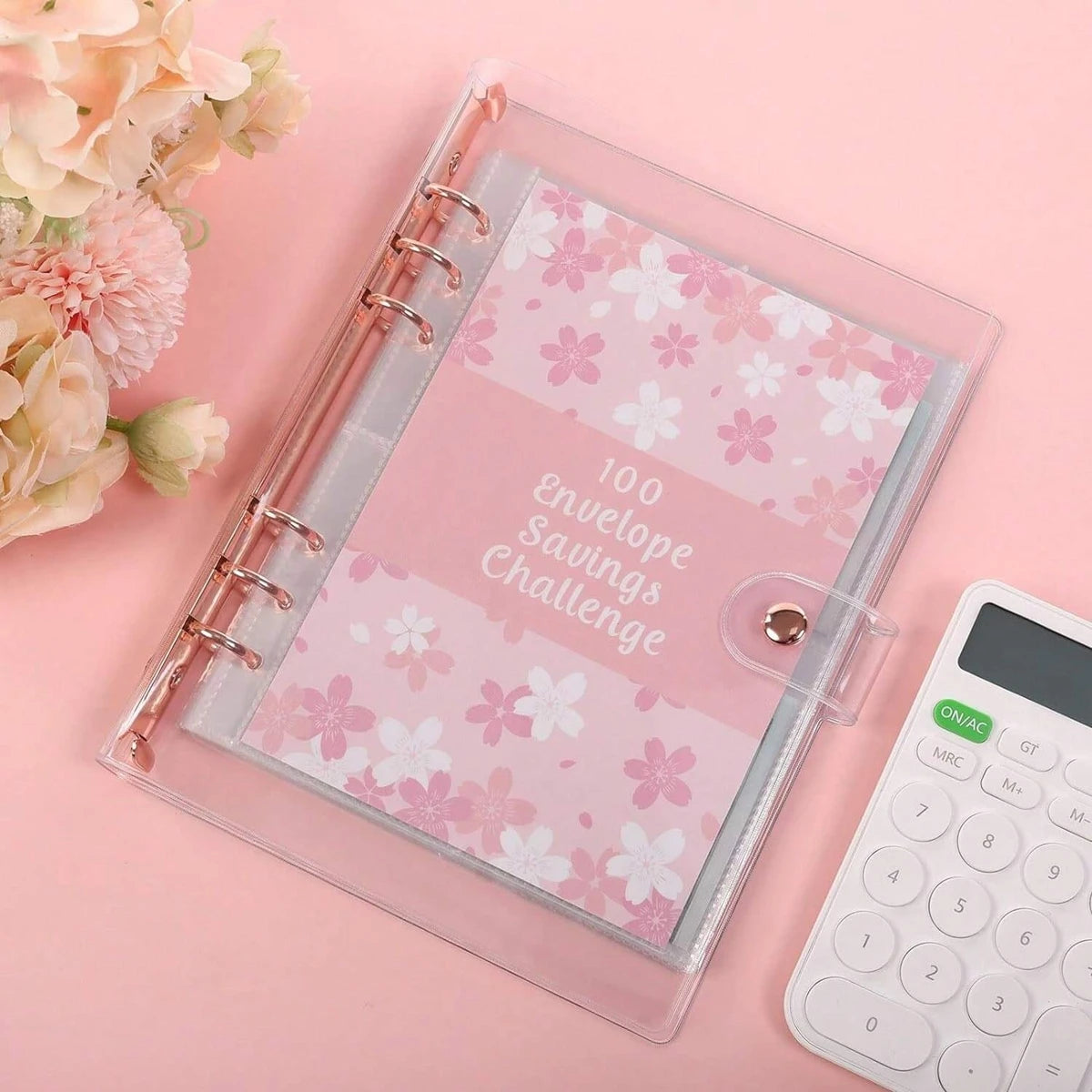 A clear plastic envelope containing a pink patterned savings challenge journal and a white calculator on a pink background.