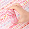 A hand holds a stack of pink butterfly and gingham washi tape rolls on a patterned fabric.