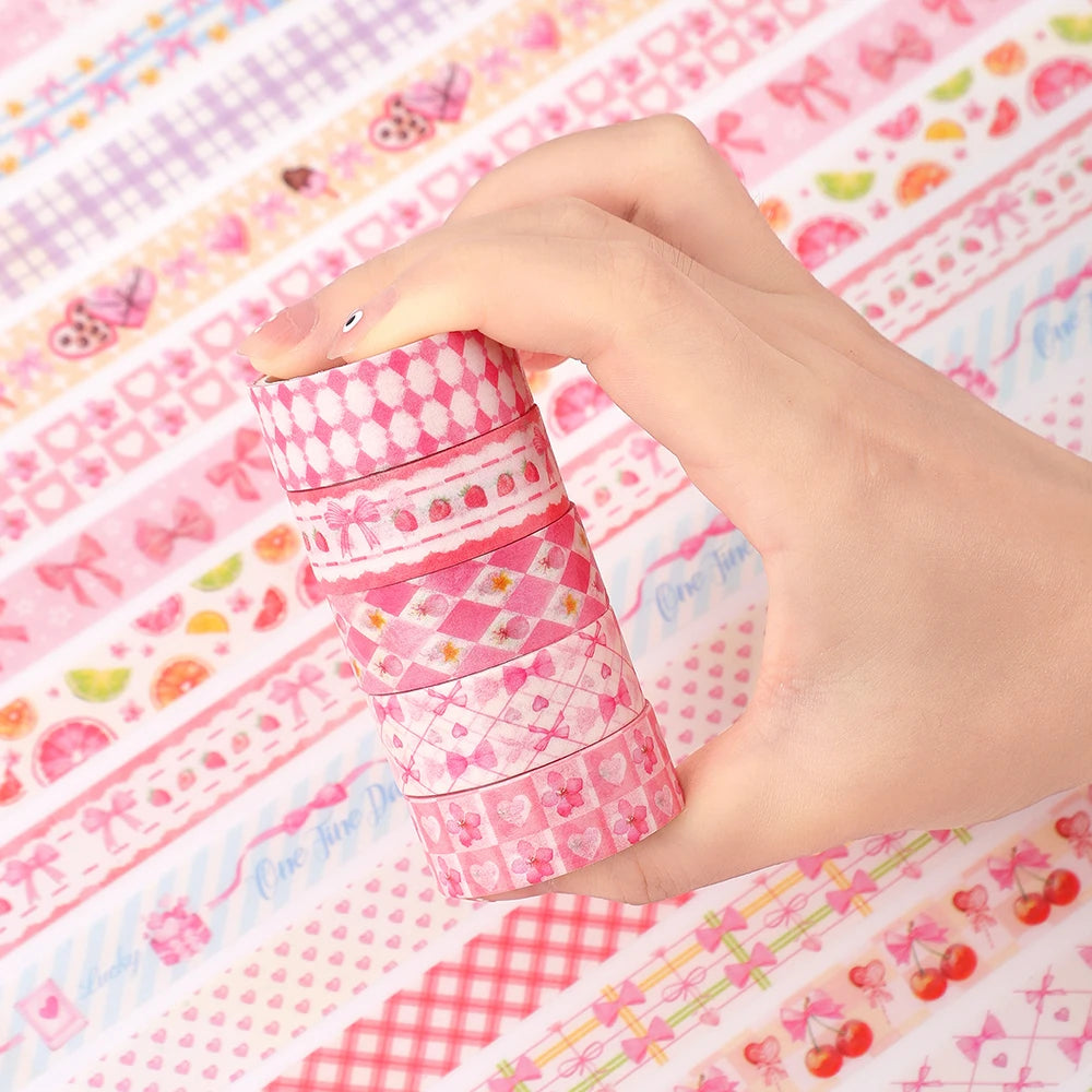 A hand holds a stack of pink butterfly and gingham washi tape rolls on a patterned fabric.