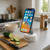 An orange foldable magnetic phone holder is displayed on a kitchen counter next to a cutting board and vegetables.