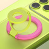 A pink and lime green phone ring holder stand is shown resting on a light green surface next to a yellow charging pad.