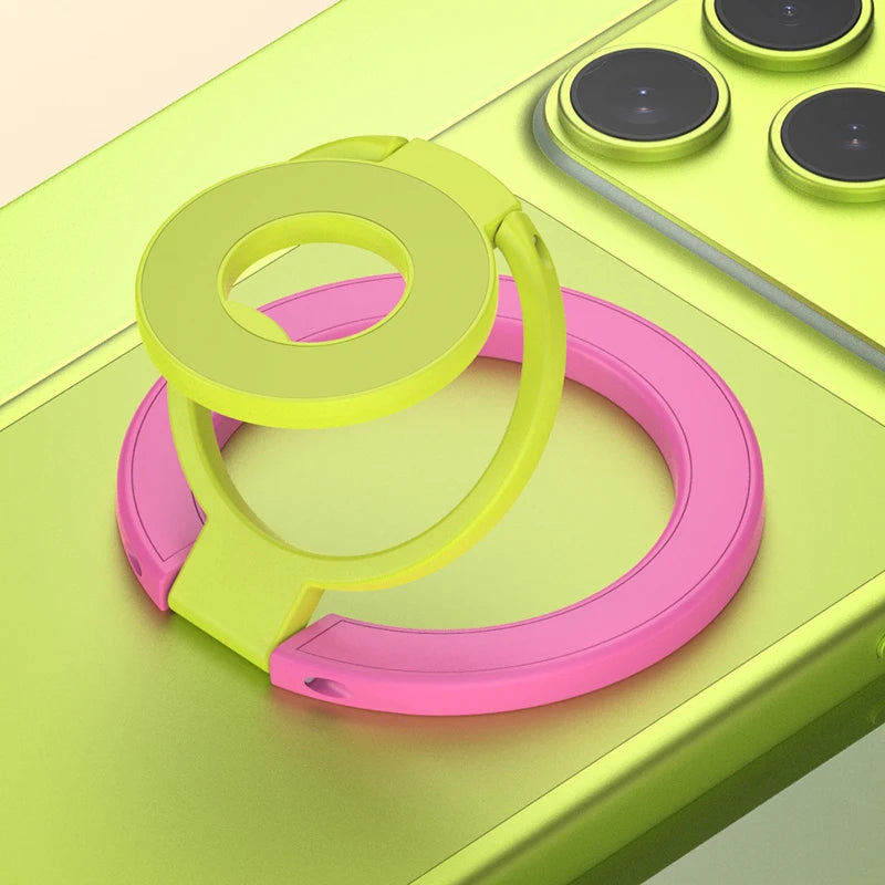 A pink and lime green phone ring holder stand is shown resting on a light green surface next to a yellow charging pad.