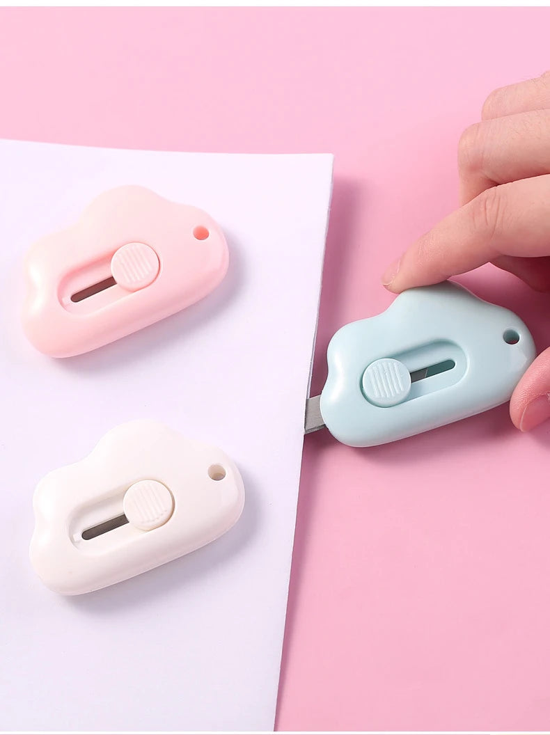 A hand holds a light pink portable utility knife next to a light blue one on a white background.