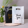 Two kraft paper gift bags, one black and one white, with gold script text saying Thank you.