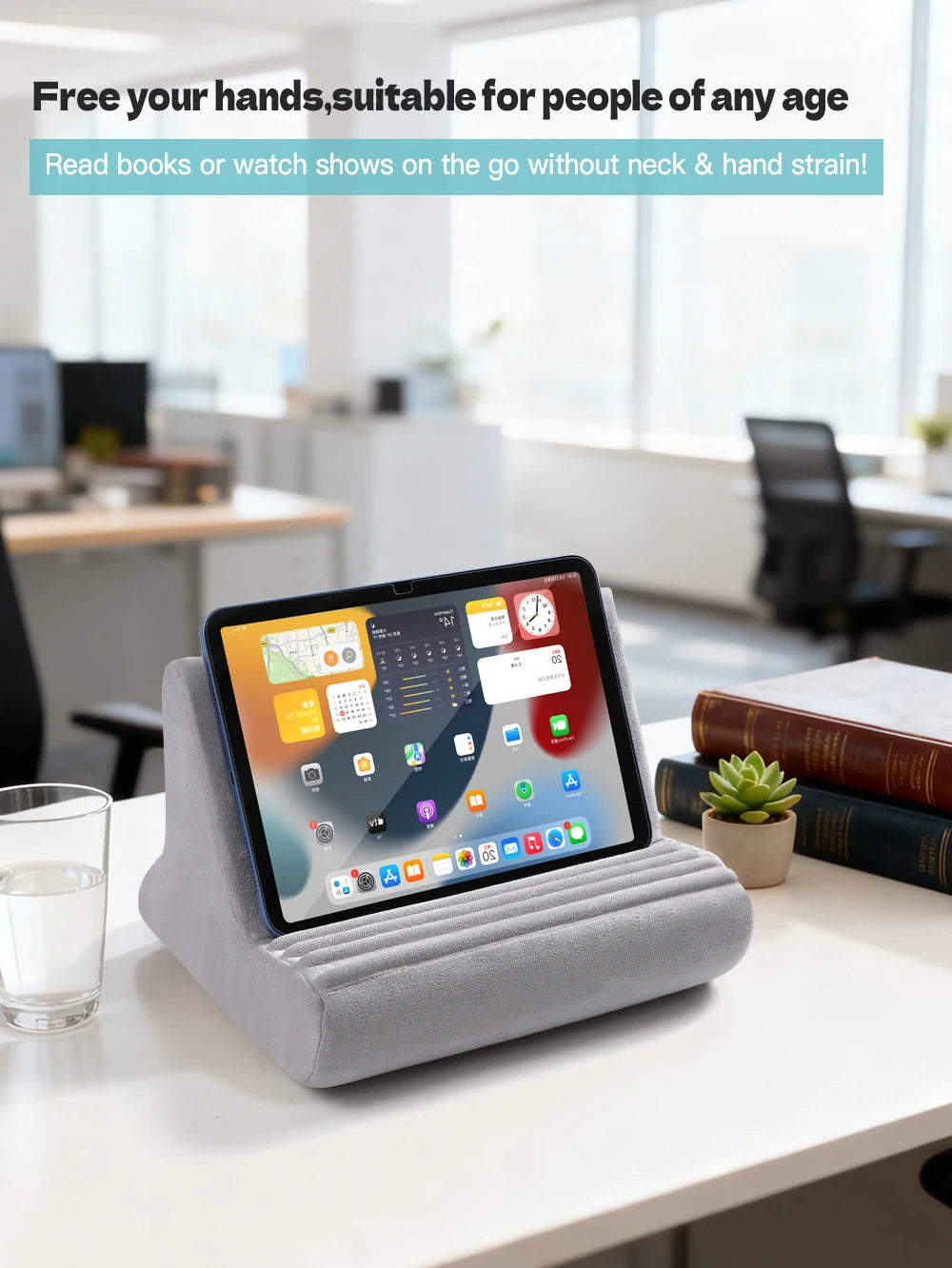 A gray multi-angle adjustable tablet and phone holder resting on a white table in an office setting.