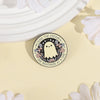A round enamel pin featuring a cute ghost character surrounded by flowers and text on a light yellow background.