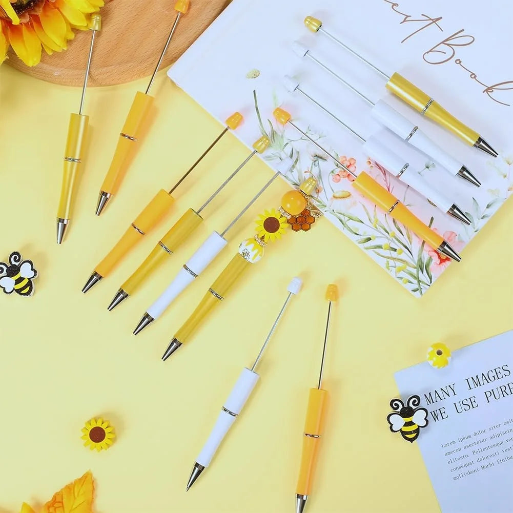 A set of yellow and white beaded pens with sunflower accents arranged on a light yellow background.