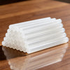 A set of white hot melt glue sticks arranged in a row on a wooden surface.