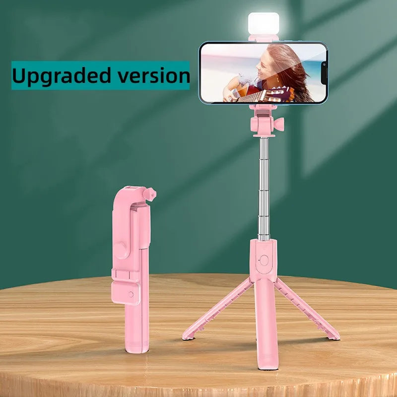 A pink selfie stick tripod with a fill light and wireless remote is displayed on a wooden surface.