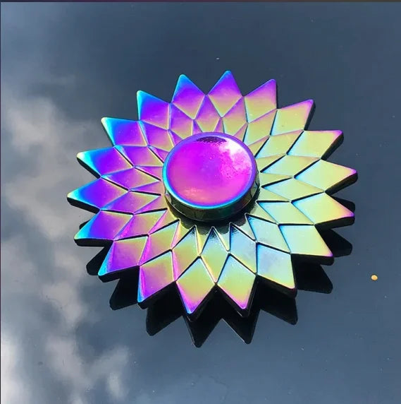 A rainbow metal fidget spinner with a multifaceted, sunburst design reflecting iridescent colors.