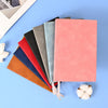 A stack of five colored leather journals or diaries, including shades of red, orange, black, gray, and blue-green, resting on