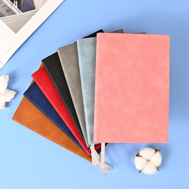 A stack of five colored leather journals or diaries, including shades of red, orange, black, gray, and blue-green, resting on