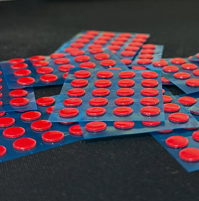 A collection of red adhesive dots on blue PTFE mouse skates arranged in a grid pattern.