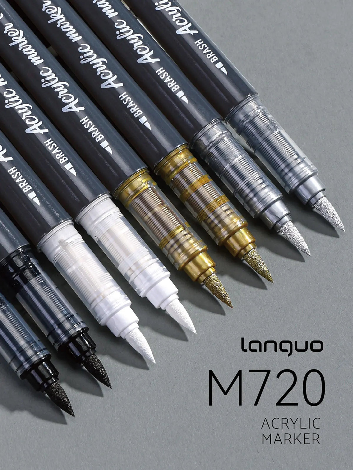 A collection of black acrylic marker pens with gold accents arranged diagonally on a gray surface.