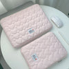 A pink quilted laptop sleeve with a white mouse is displayed on a white table.
