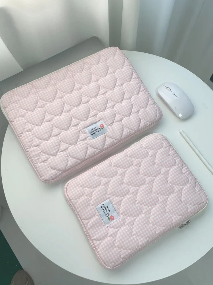 A pink quilted laptop sleeve with a white mouse is displayed on a white table.