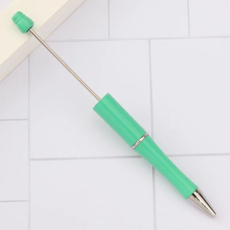 A bright green DIY beadable pen with a silver tip and a metal cap resting on a white tiled surface.