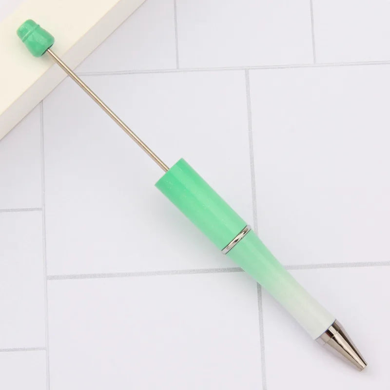 A green DIY beadable pen with a silver clip is shown lying on a white surface.