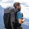 A man wearing a blue shirt and backpack looks out over a scenic landscape.