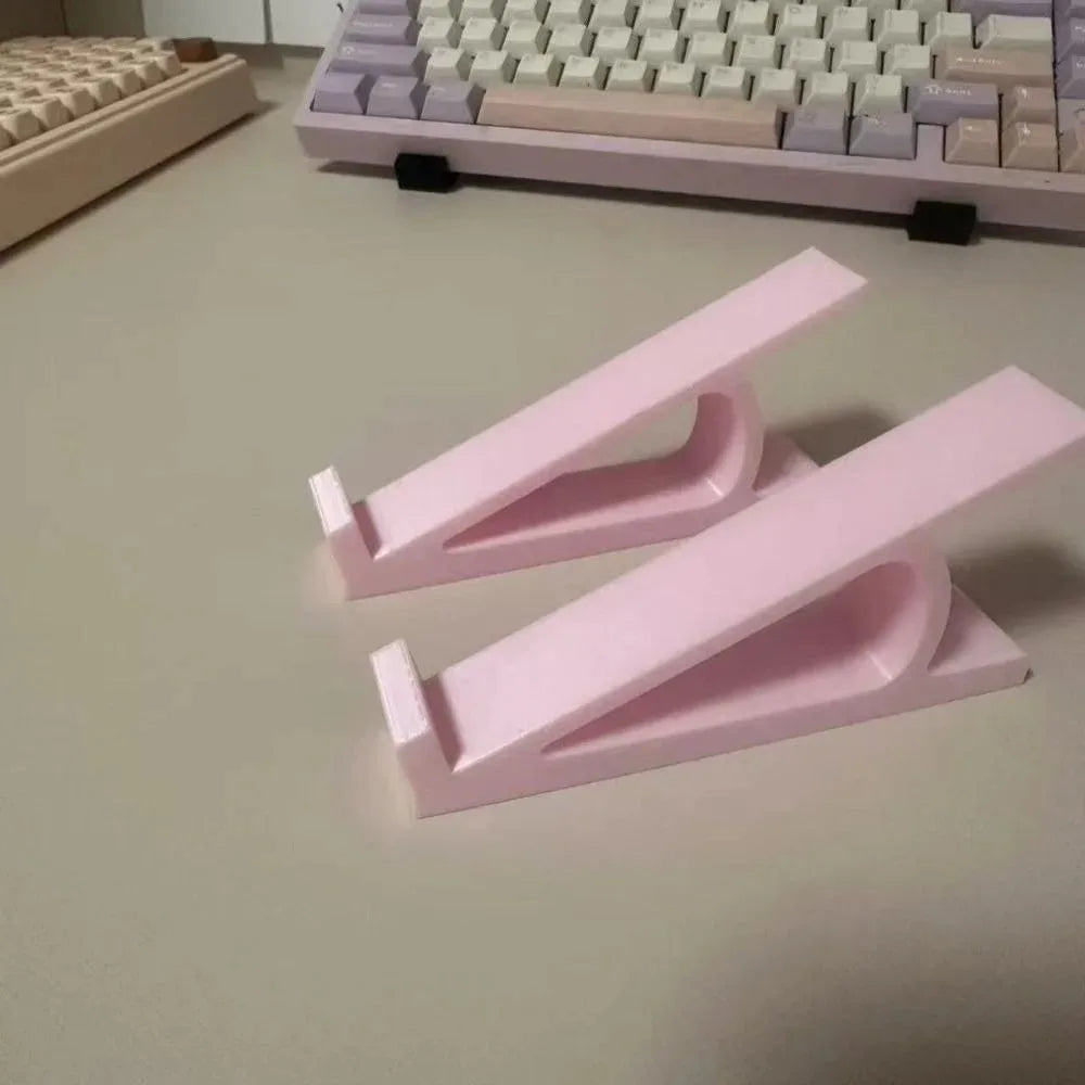 Pink ergonomic keyboard height adjuster stand with two adjustable pink plastic pieces on a light surface.