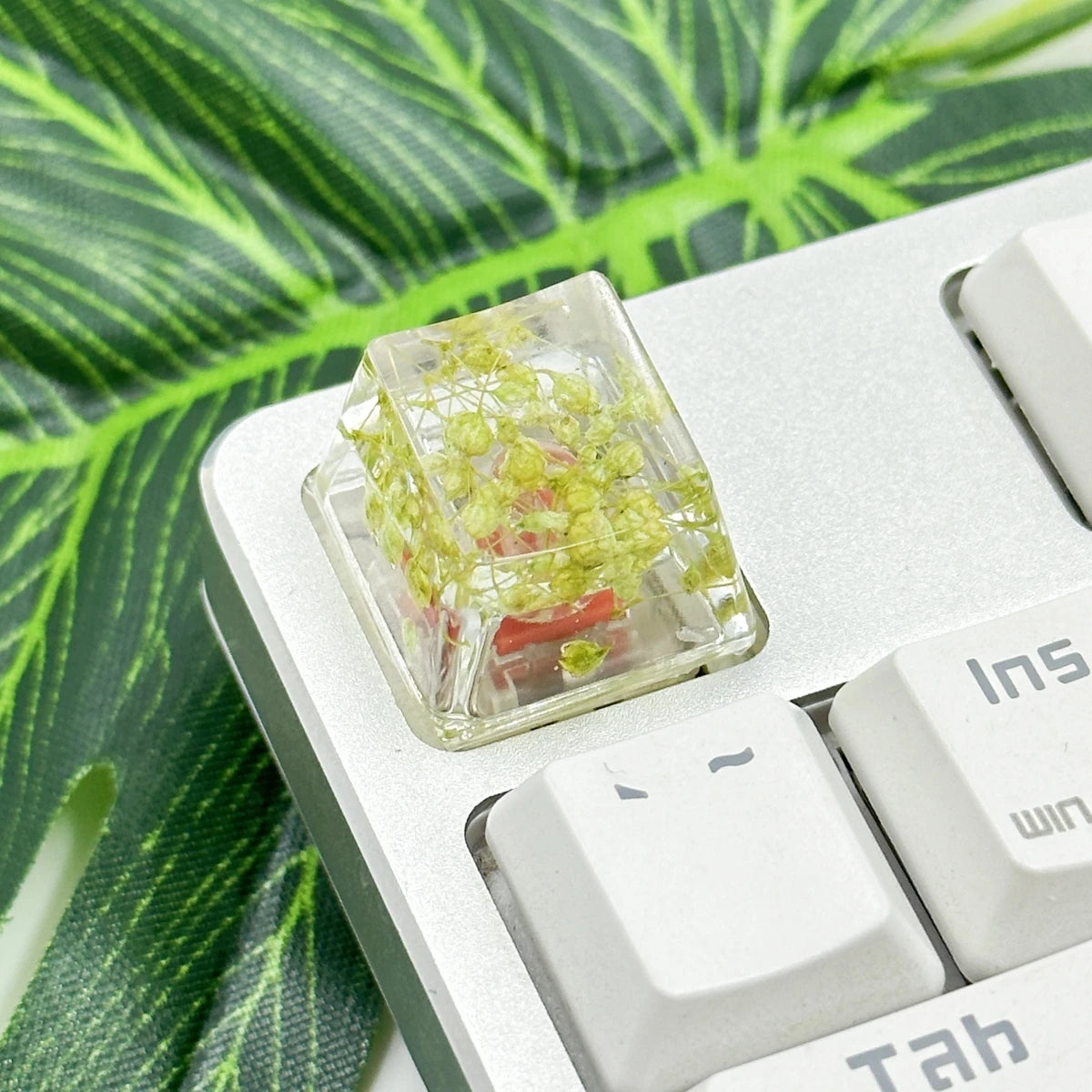 Translucent botanical resin keycaps with small green plant material resting on a mechanical keyboard.