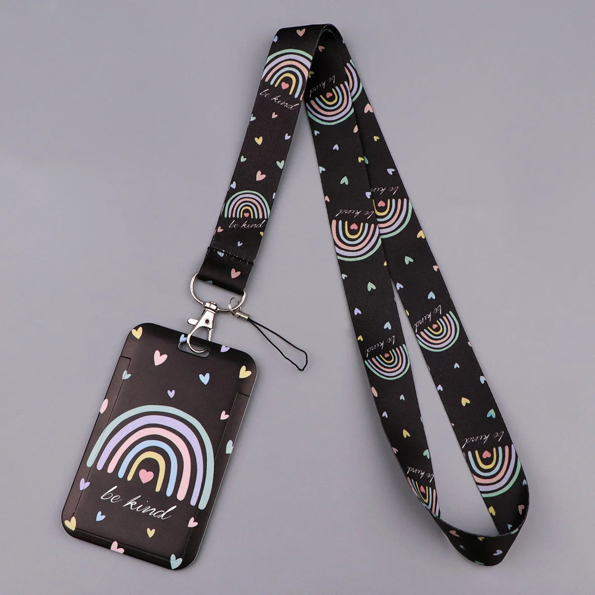 A black minimalist heart-shaped lanyard featuring a rainbow pattern and the text be kind