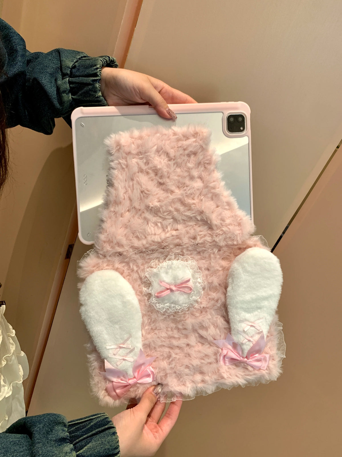A pink rabbit plush case is being held by a person against a light-colored wall.