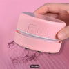 Eine Hand hält einen rosa Mini-Tischstaubsauger, der zum Reinigen von Papier und Staub dient.